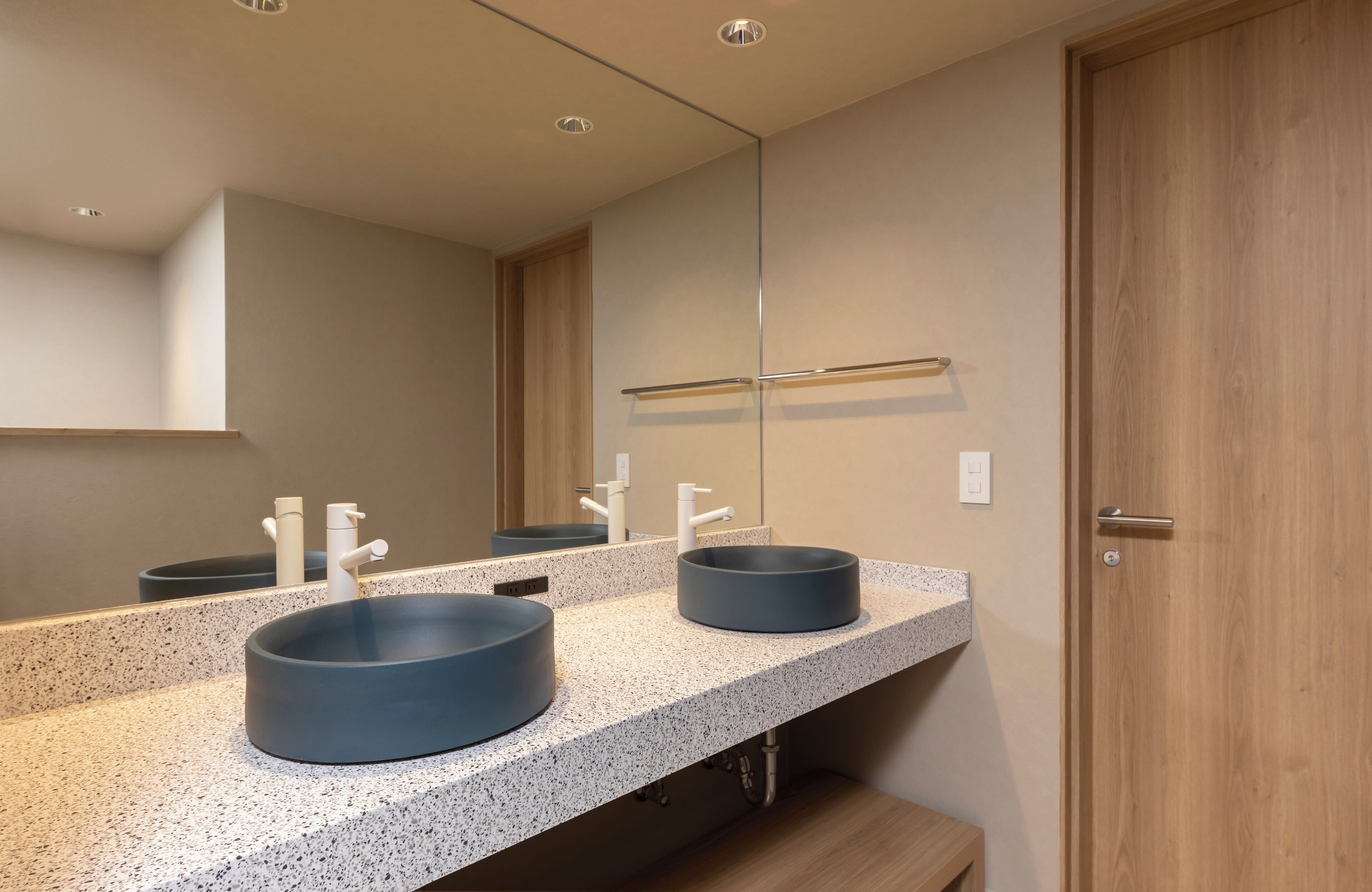 A modern bathroom with two round sinks, a large mirror, and a wooden door.
