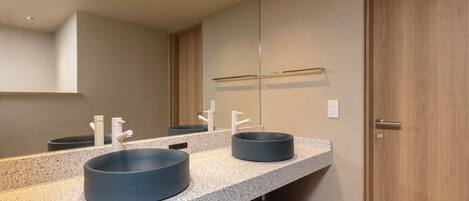 A modern bathroom with two round sinks, a large mirror, and a wooden door.