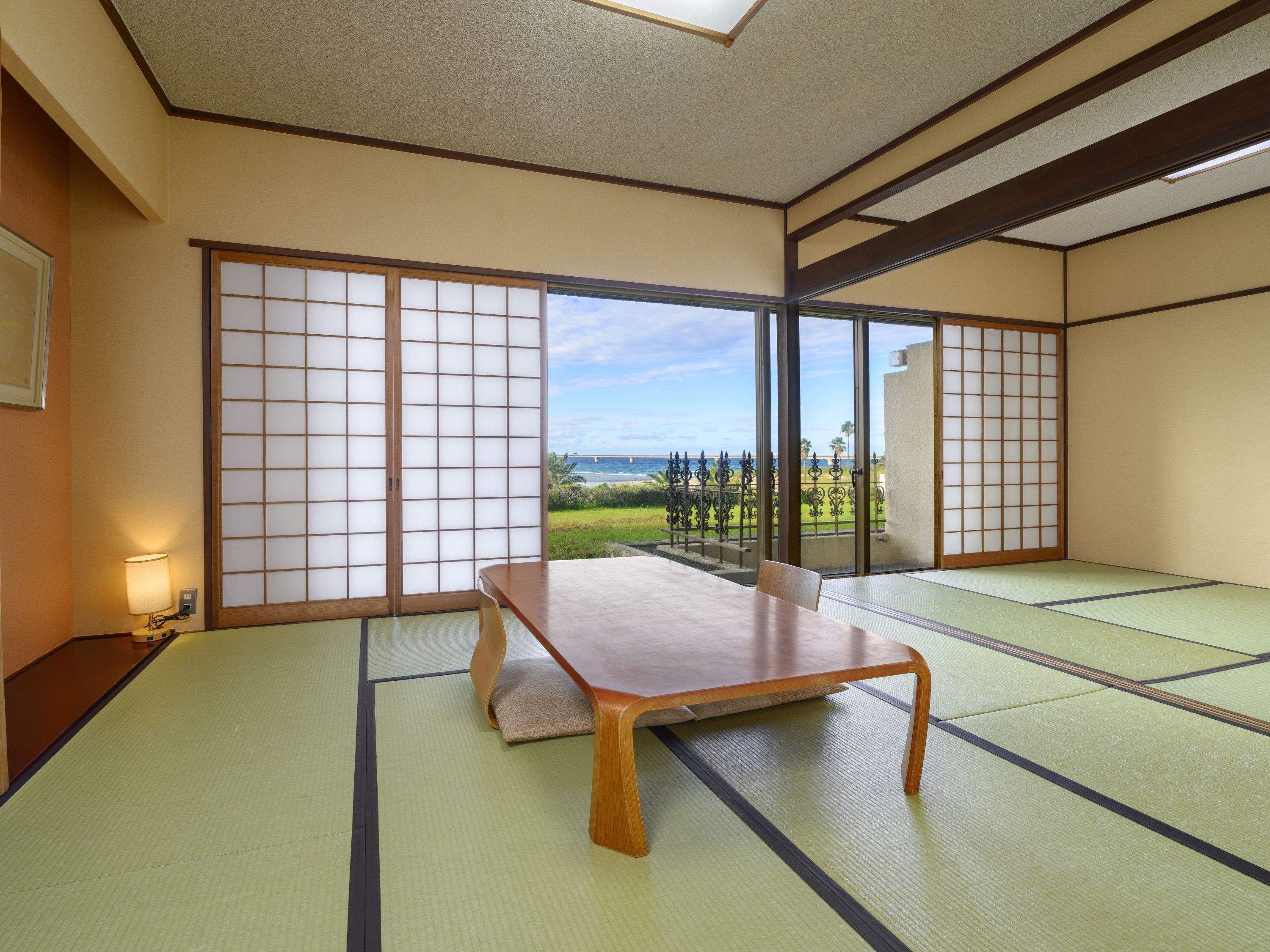 A tatami mat room with a sliding door leading to a balcony with a view of the beach and ocean.