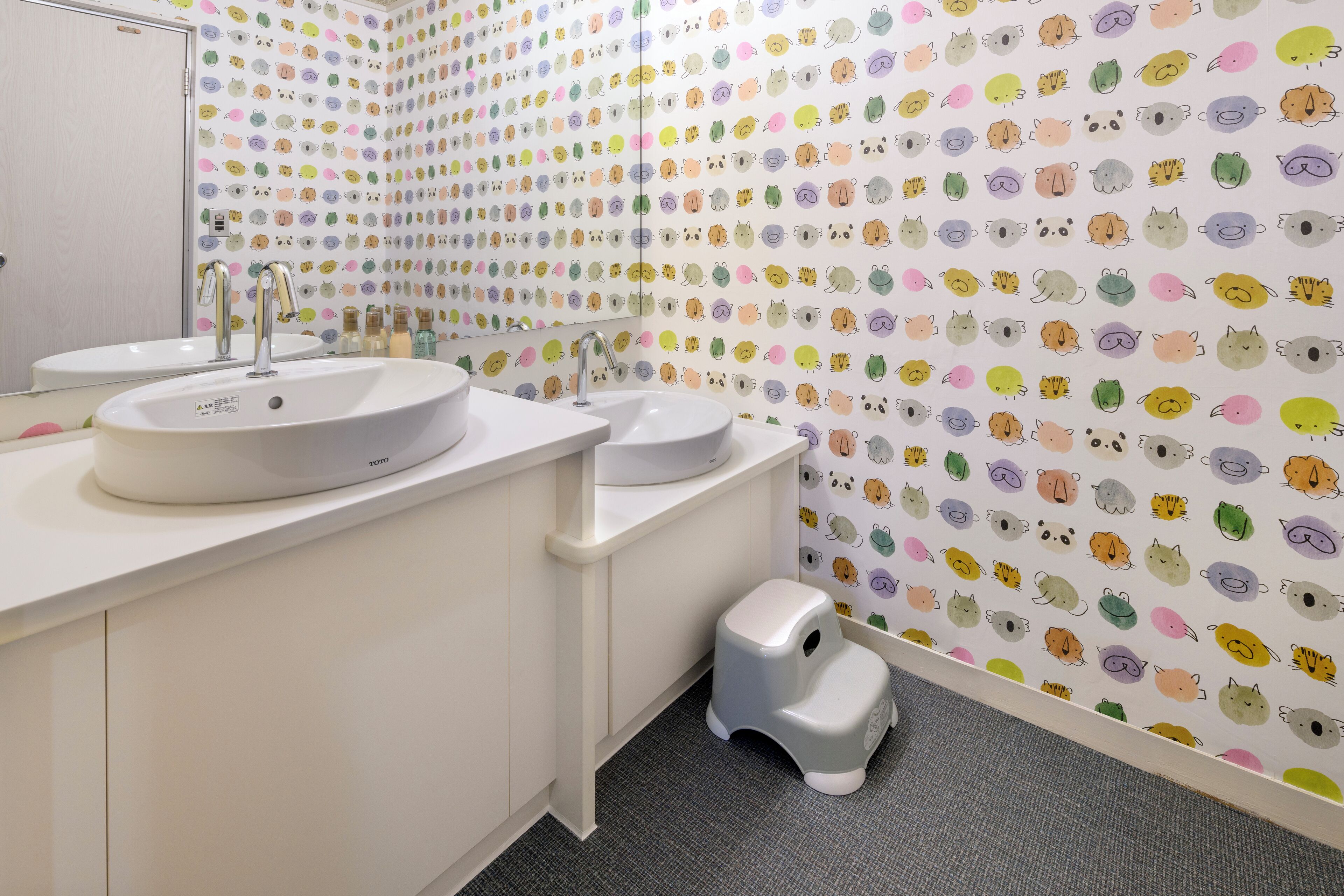 Un baño con dos lavamanos, un espejo y un papel tapiz con motivos de animales.