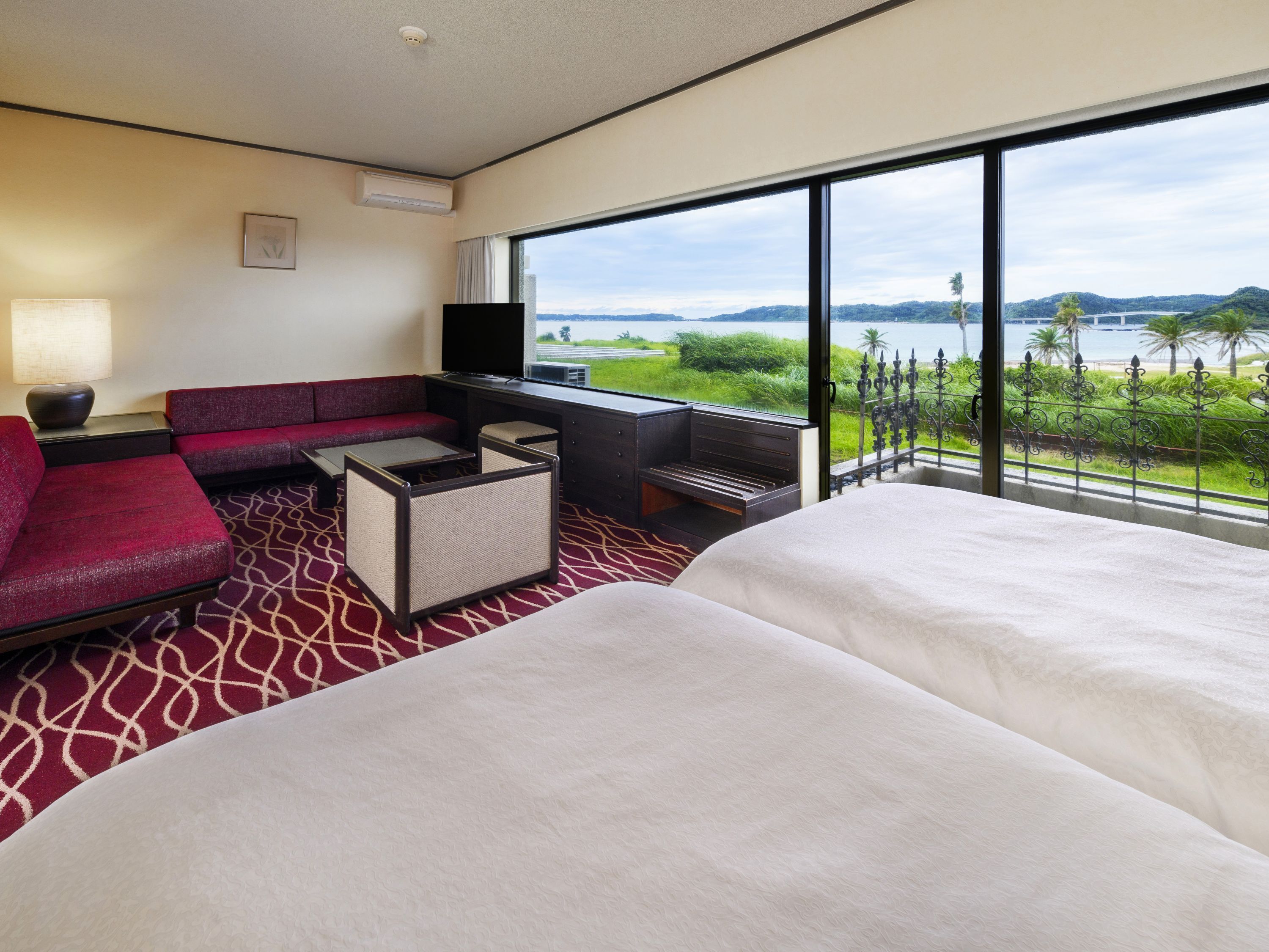 A hotel room with a large window, a sofa, a TV, and a bed.