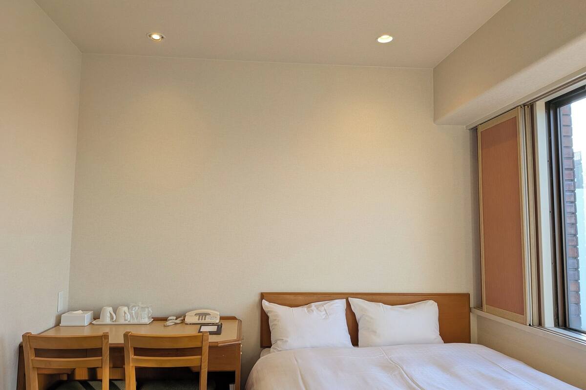 A hotel room with a bed, a desk with a telephone, and a window.