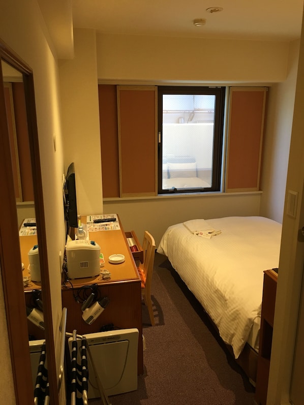 Una habitación de hotel con una cama, un escritorio con una computadora, una silla y una ventana.