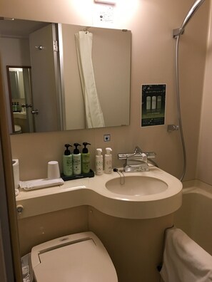 A bathroom with a sink, mirror, shower, and toilet. There are toiletries on the sink counter. - Smile Hotel Sugamo (Tokyo)