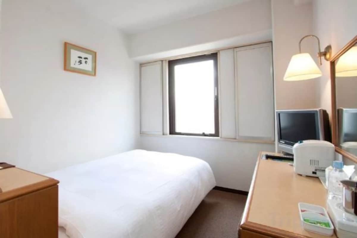 Una habitación de hotel con una cama, un escritorio con una computadora, una lámpara y una ventana.