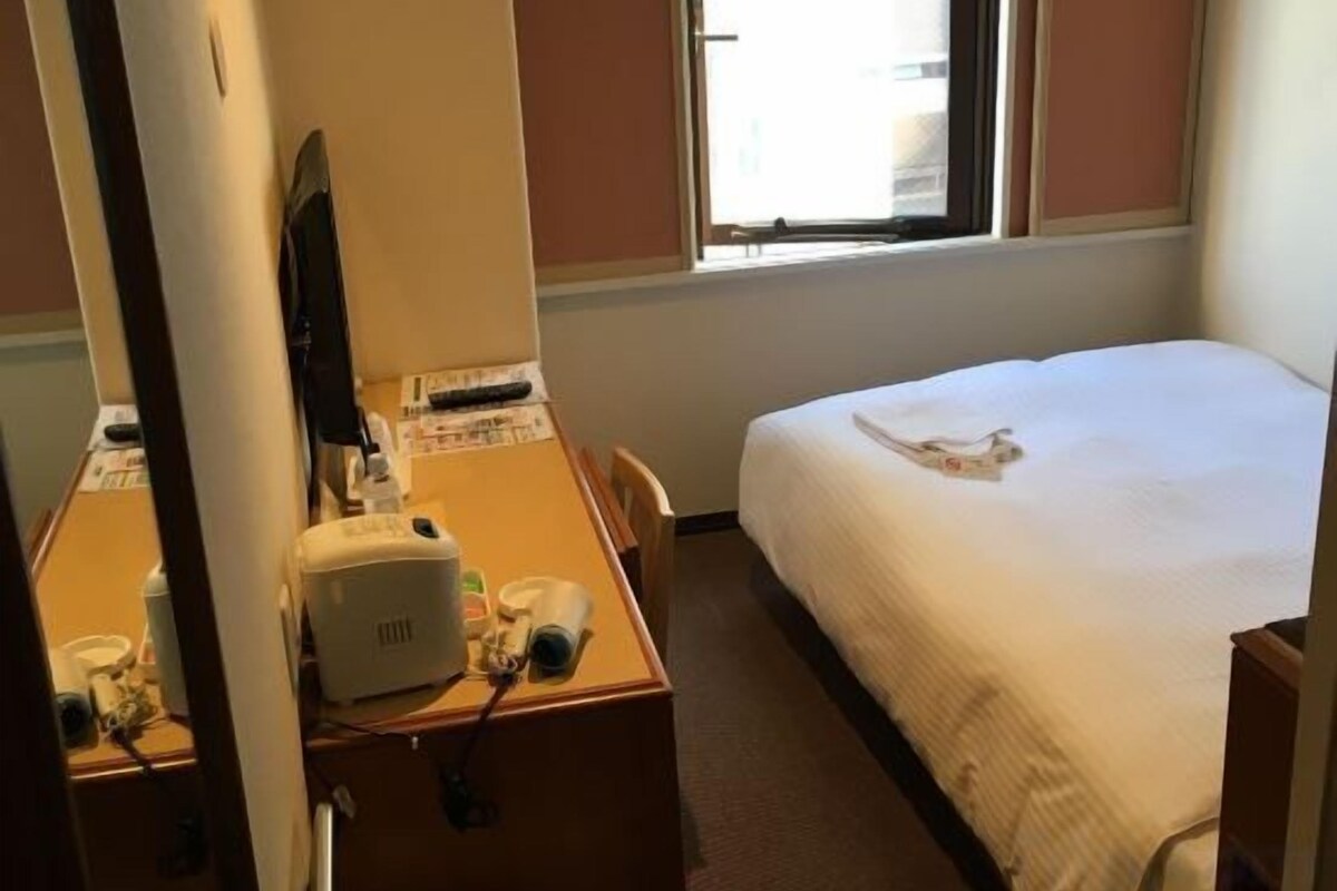 Ett hotellrum med en säng, ett skrivbord med en dator och ett fönster.
