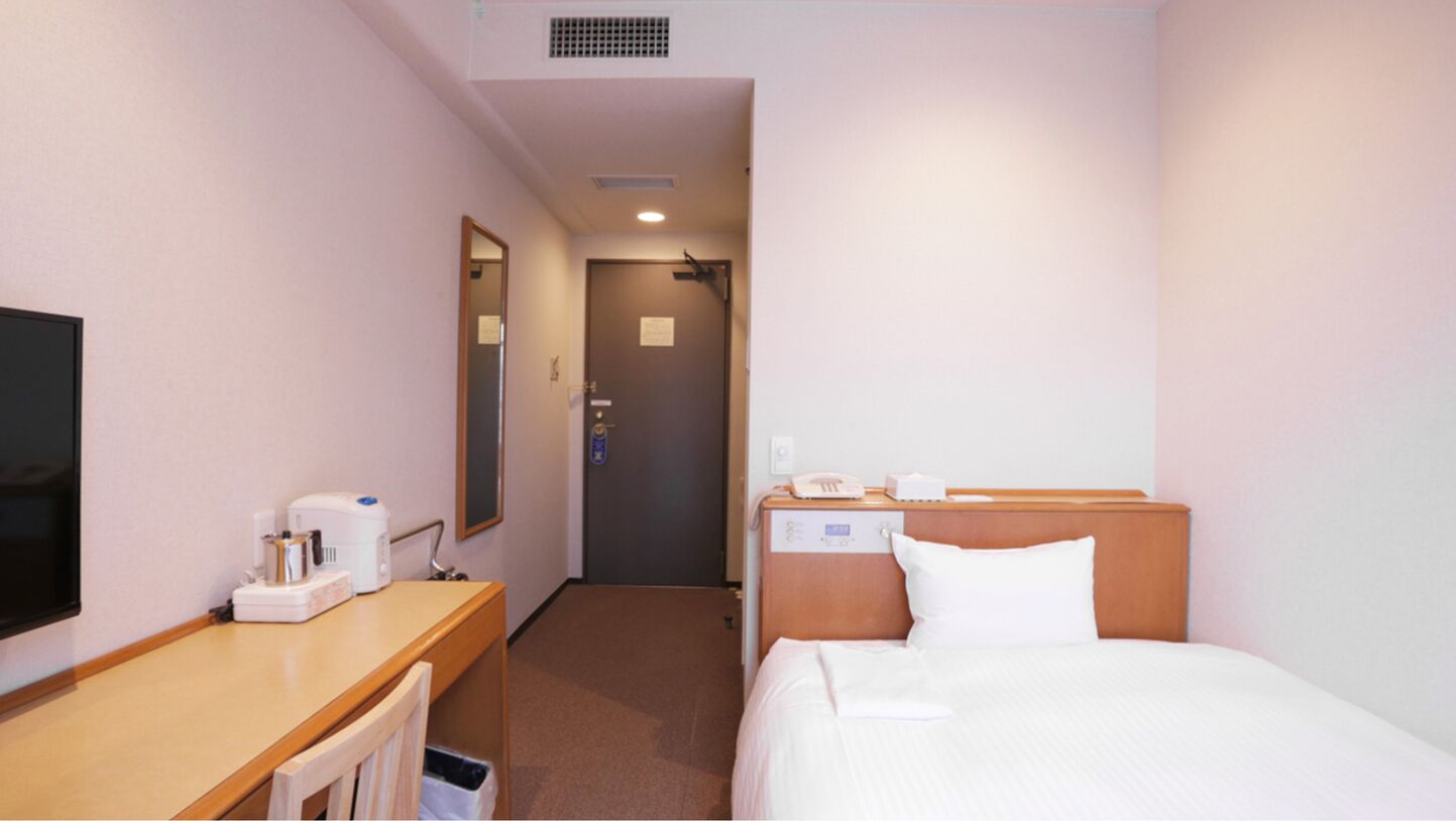 A hotel room with a bed, bedside table, a television, and a mirror.