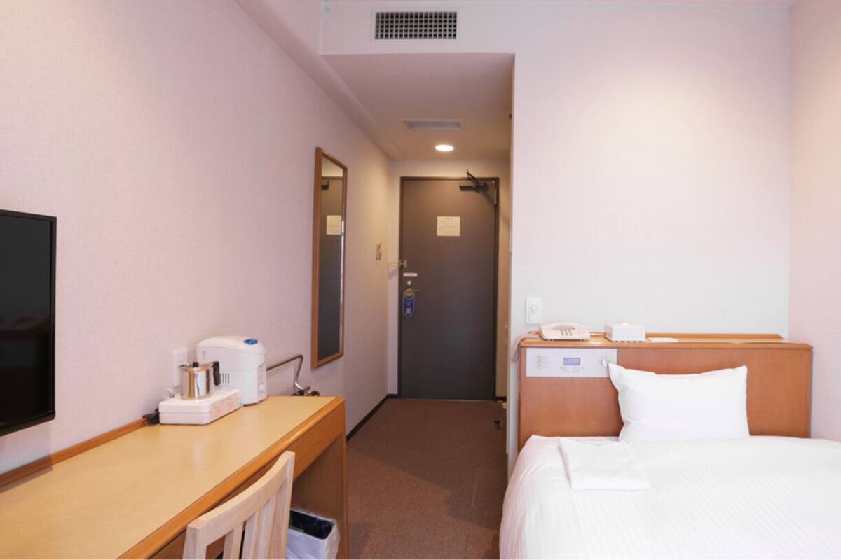 A hotel room with a bed, bedside table, a television, and a mirror.