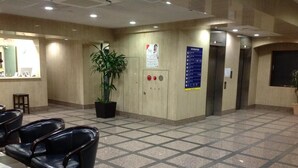 A waiting area with a tiled floor, black leather chairs, a potted plant, a reception desk, and an elevator.