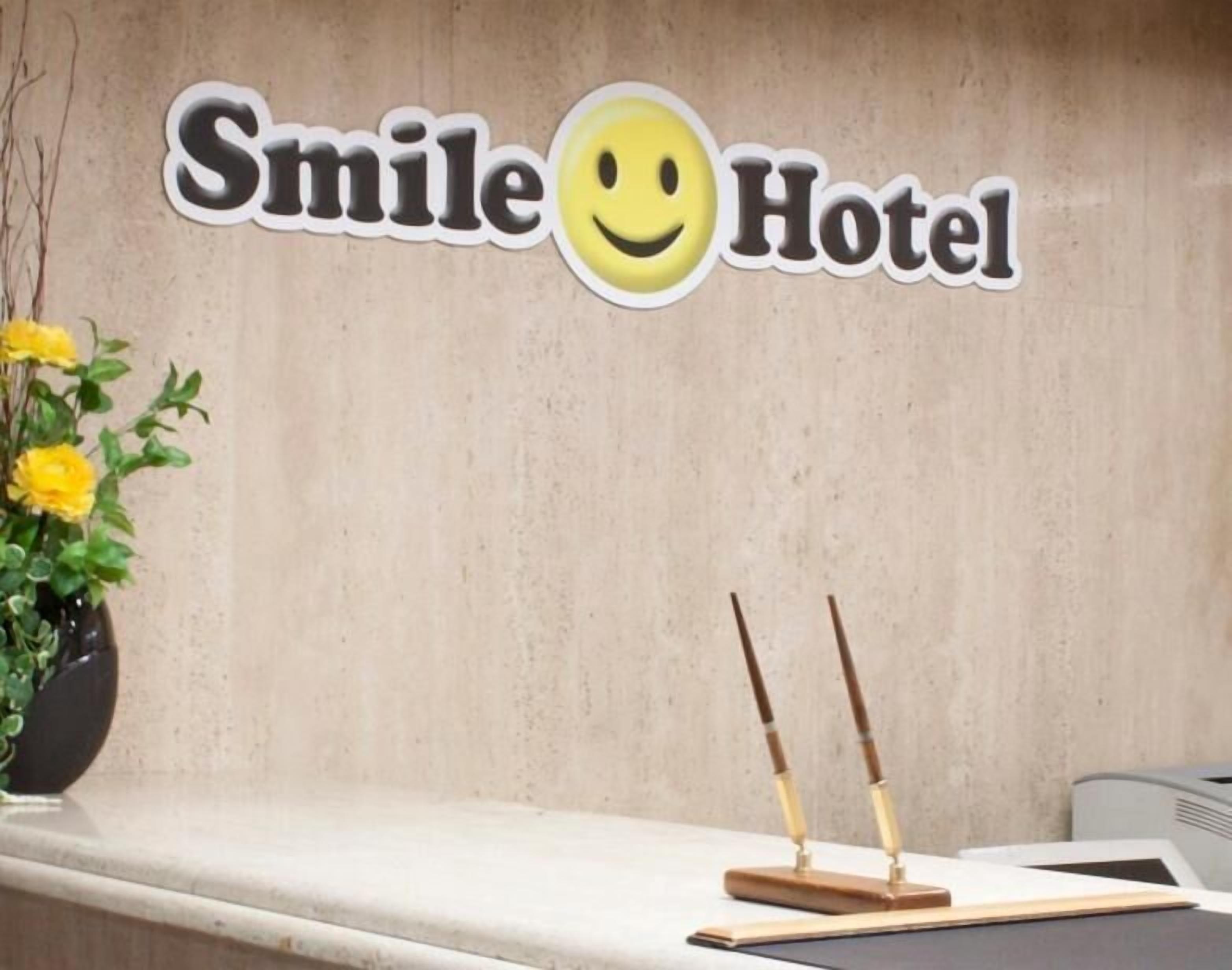 A reception desk with a sign that reads "Smile Hotel" and a yellow flower arrangement to the left.