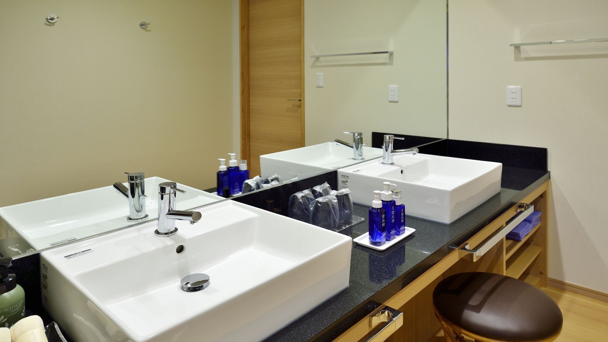 A bathroom with two white sinks, a mirror, and a wooden chair.