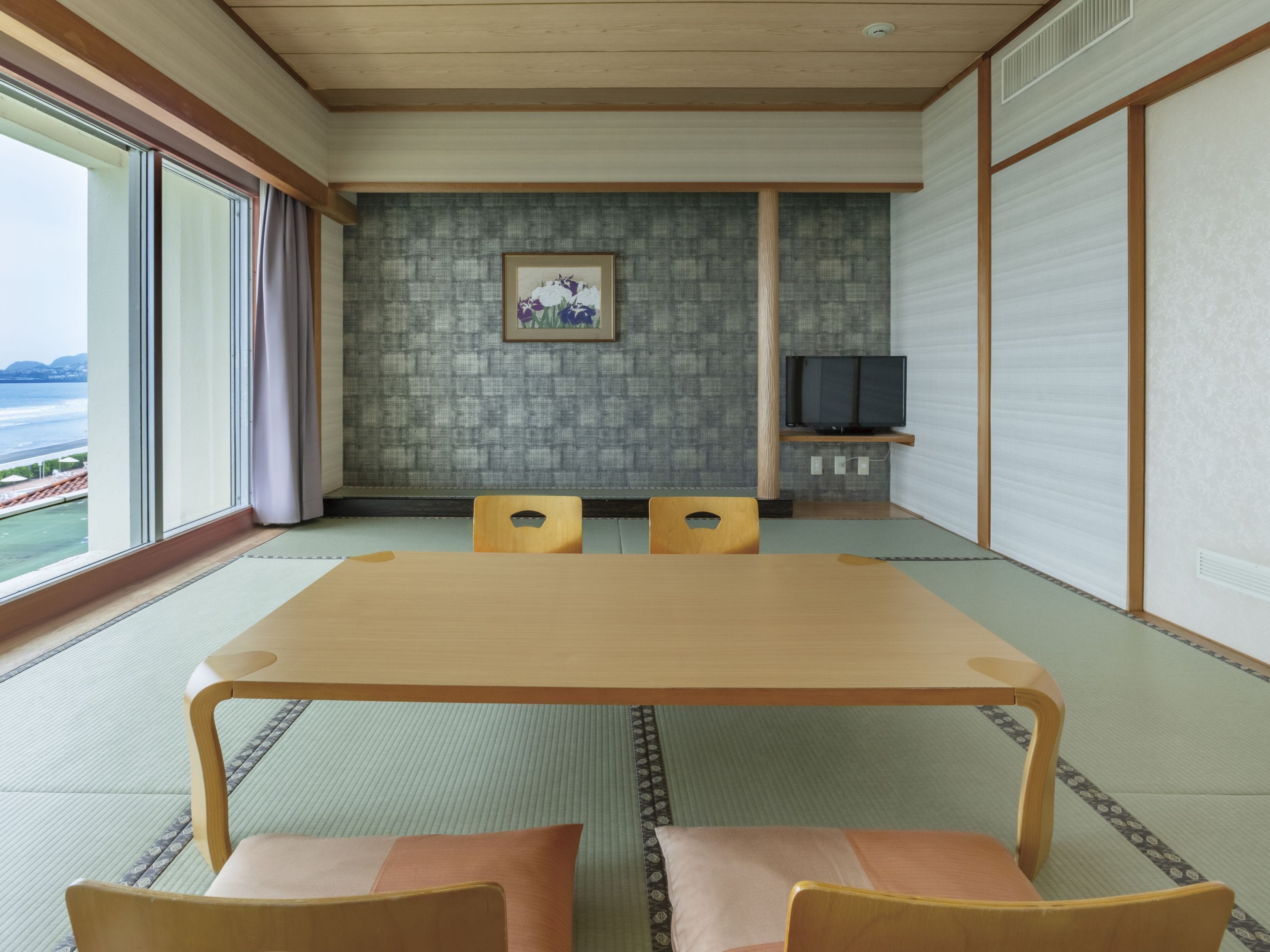 Una tradizionale stanza giapponese con pavimento in tatami, un tavolino e un televisore su uno scaffale.