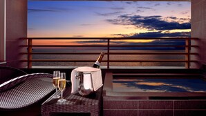 Ein Balkon mit Blick auf den Sonnenuntergang über dem Meer, eine Champagnerflasche und zwei Gläser auf einem Tisch.