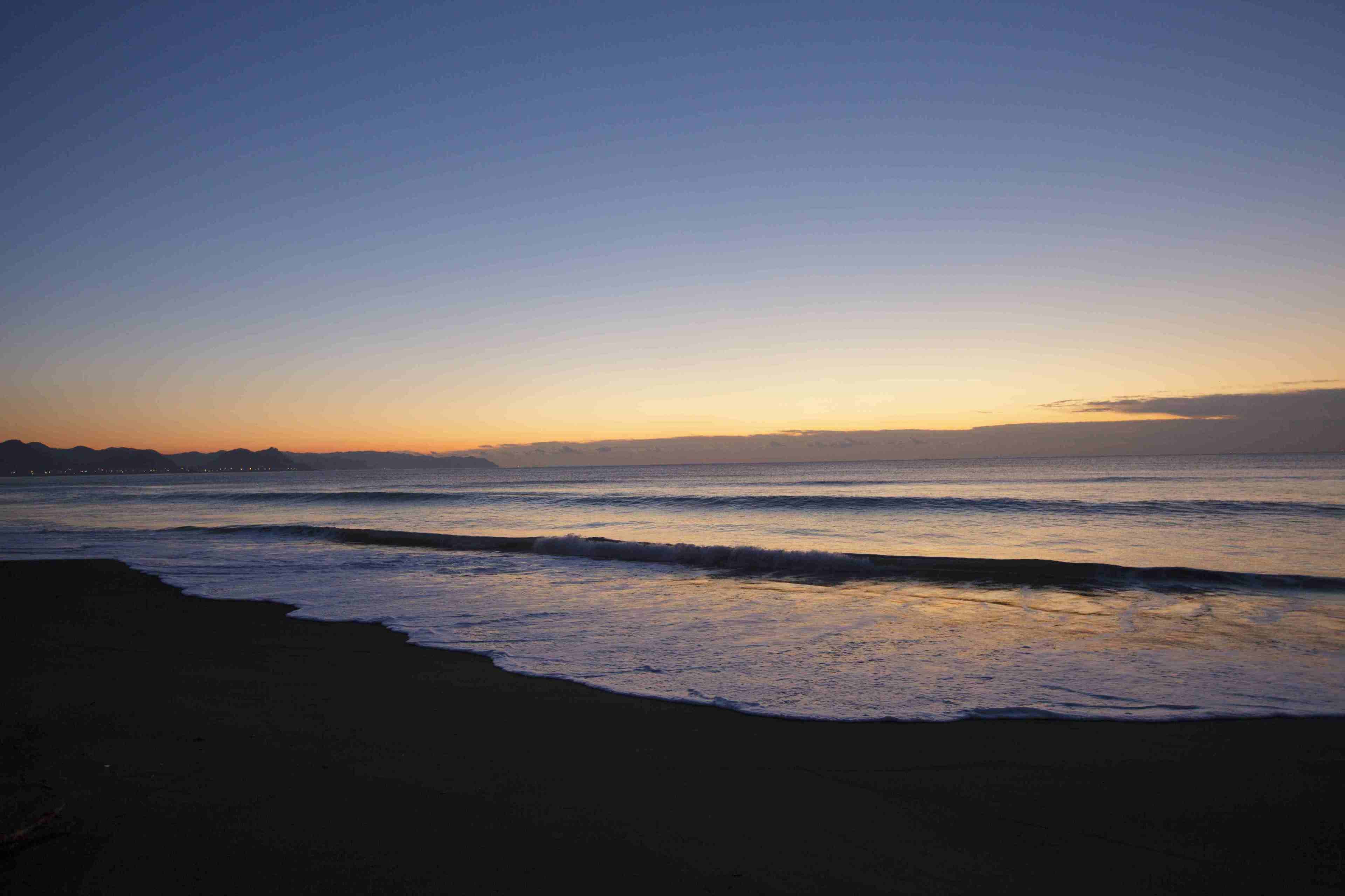 A beach at sunset with waves approaching the shore.