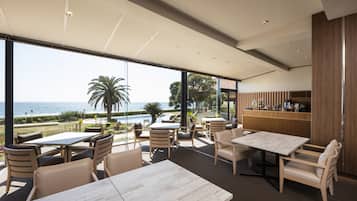 A modern outdoor dining area with tables and chairs, overlooking a pool and a view of the sea.