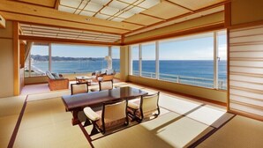 Ein geräumiges Zimmer mit einem großen Holztisch, bequemen Sitzgelegenheiten und großen Fenstern mit Blick aufs Meer.