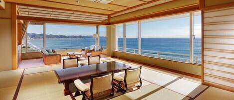 A spacious room with a large wooden table, comfortable seating, and large windows offering a view of the sea.