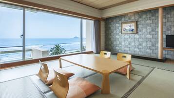 A room with tatami flooring, a wooden table, and chairs, with a view of the ocean through large windows.