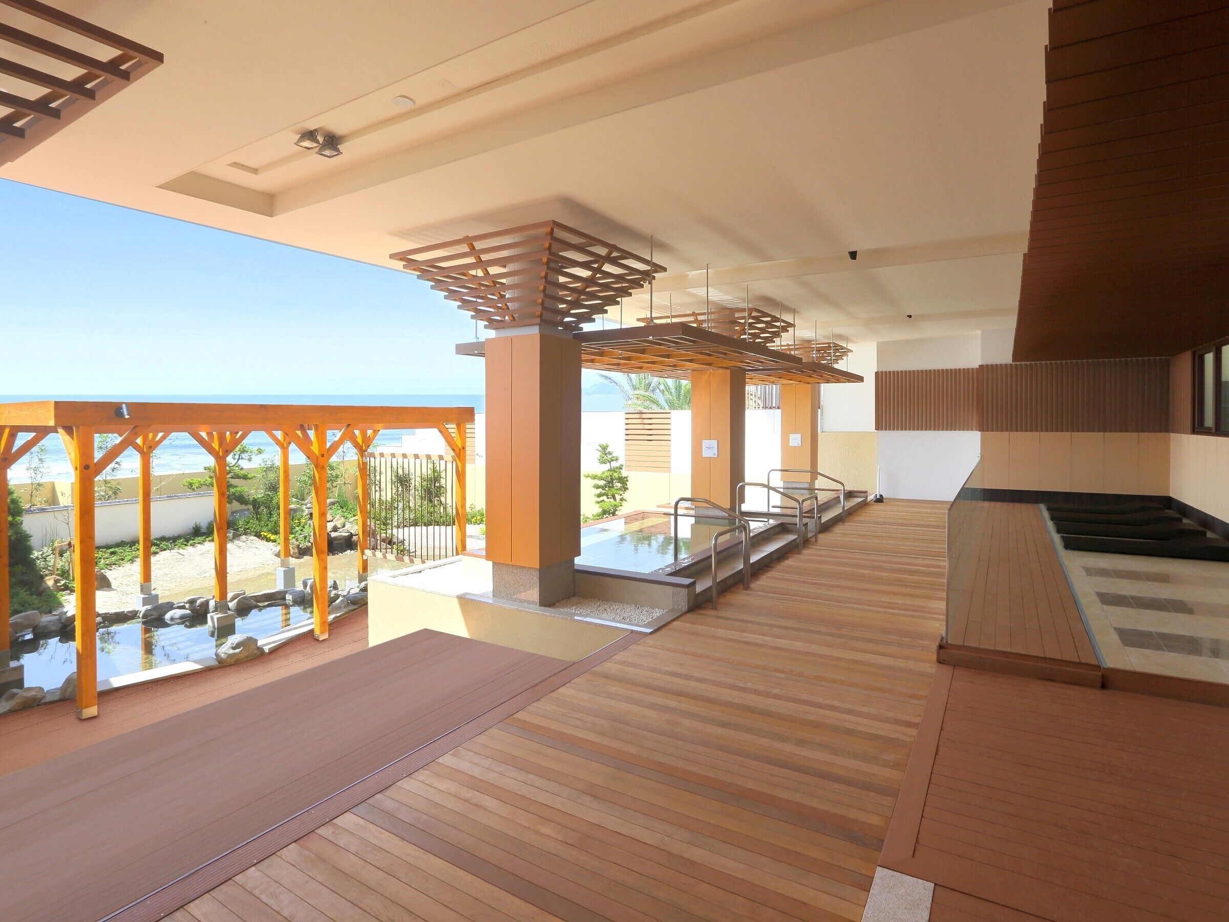Un espace piscine intérieur moderne, doté d’un plancher en bois, d’une paroi en verre et offrant une vue sur l’océan.