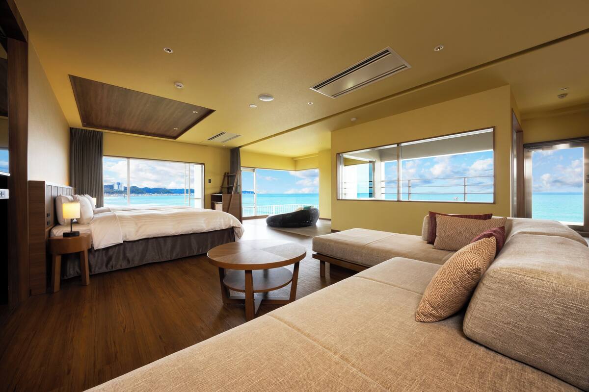Een moderne hotelkamer met een groot bed, een bank, een tafeltje en uitzicht op zee.