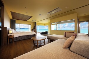 Quarto de hotel moderno com uma cama grande, um sofá, uma mesa pequena e vista para o mar.