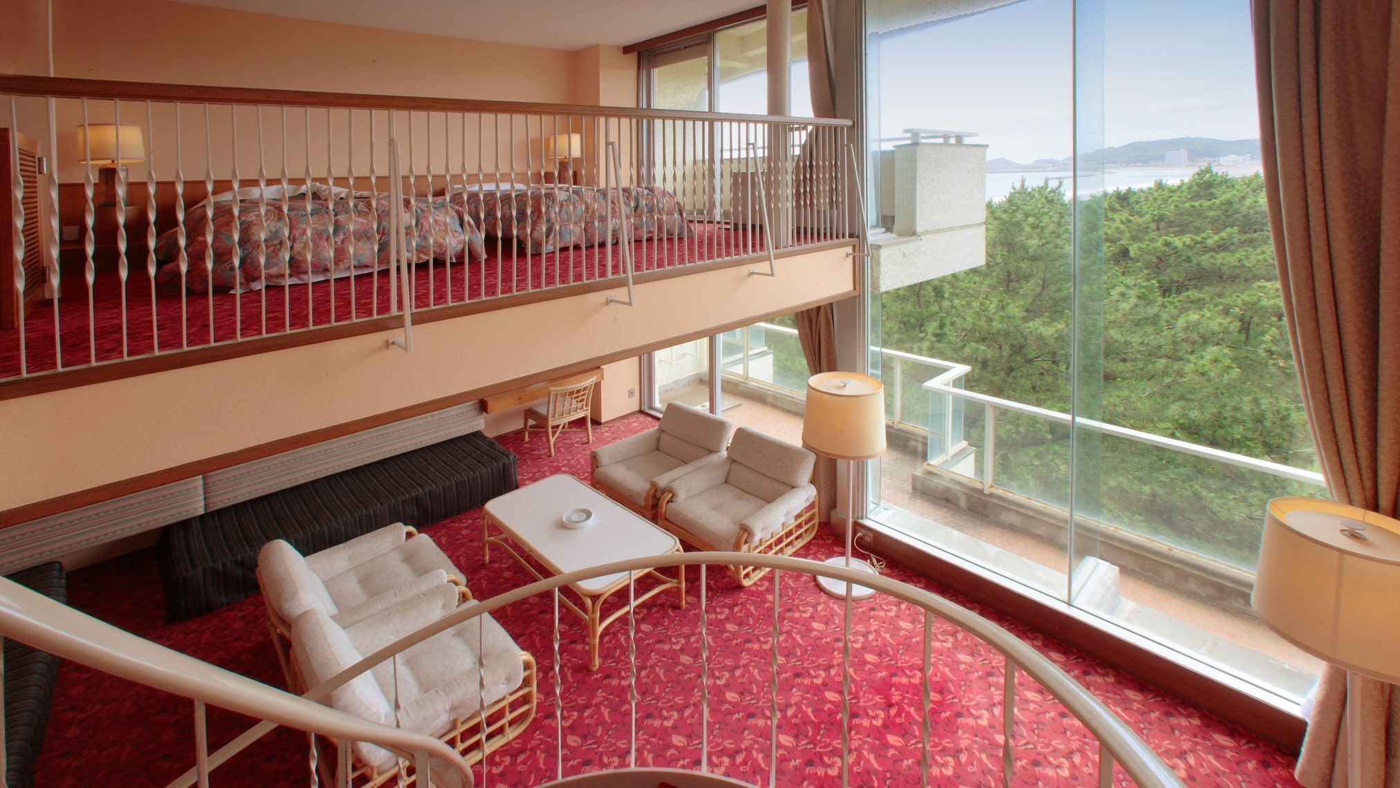 A hotel room with a balcony, a sofa, two armchairs, a small table, and a view of the outdoors.