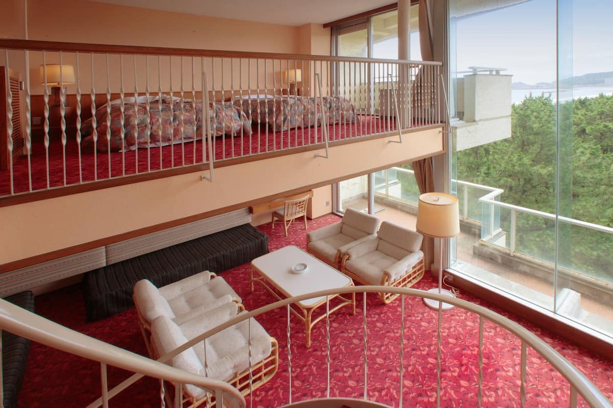 Une chambre d’hôtel avec un balcon, un canapé, deux fauteuils, une petite table et une vue sur l’extérieur.
