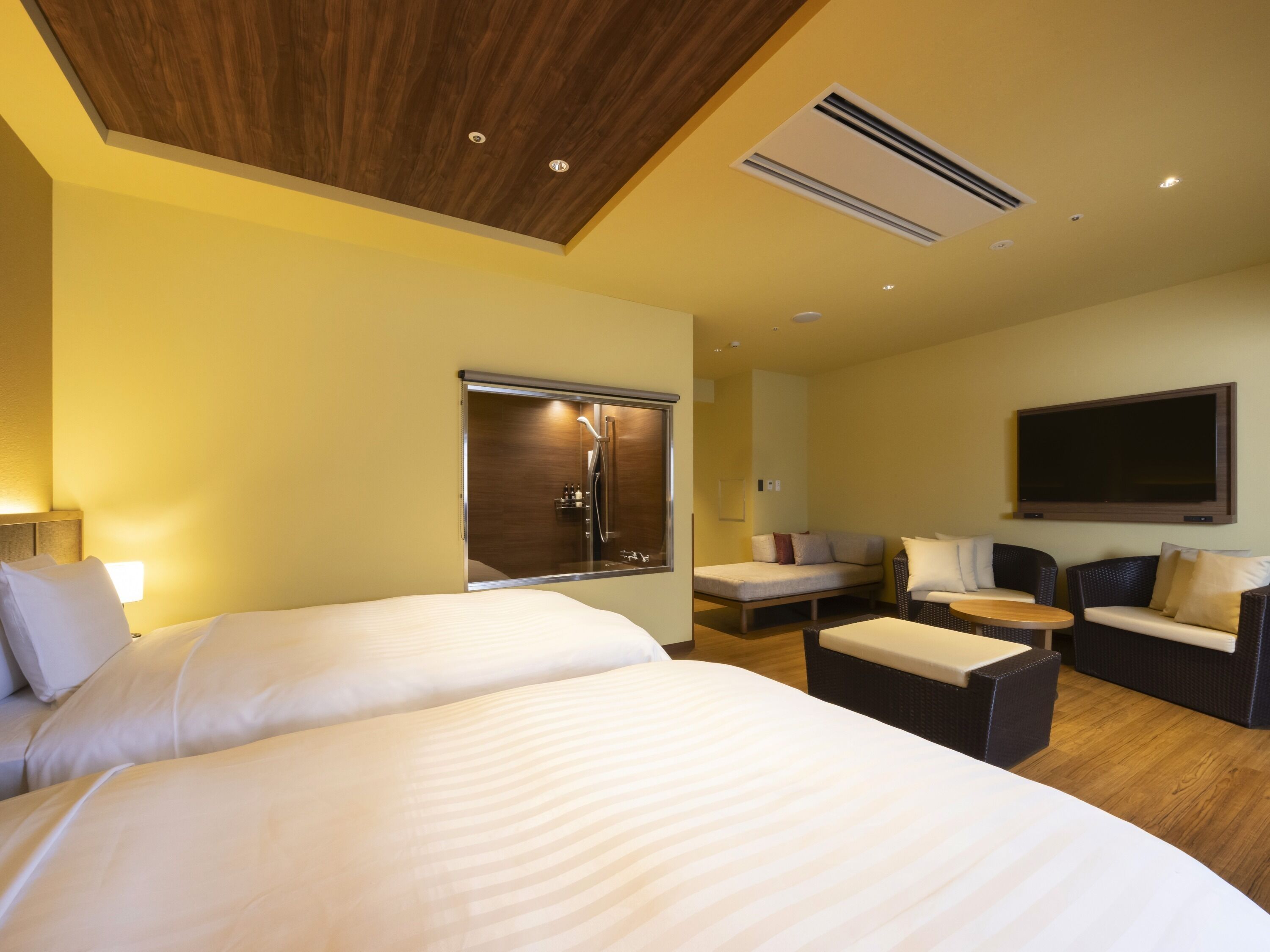 Habitación de hotel con dos camas, un sofá, un televisor y un techo con paneles de madera.