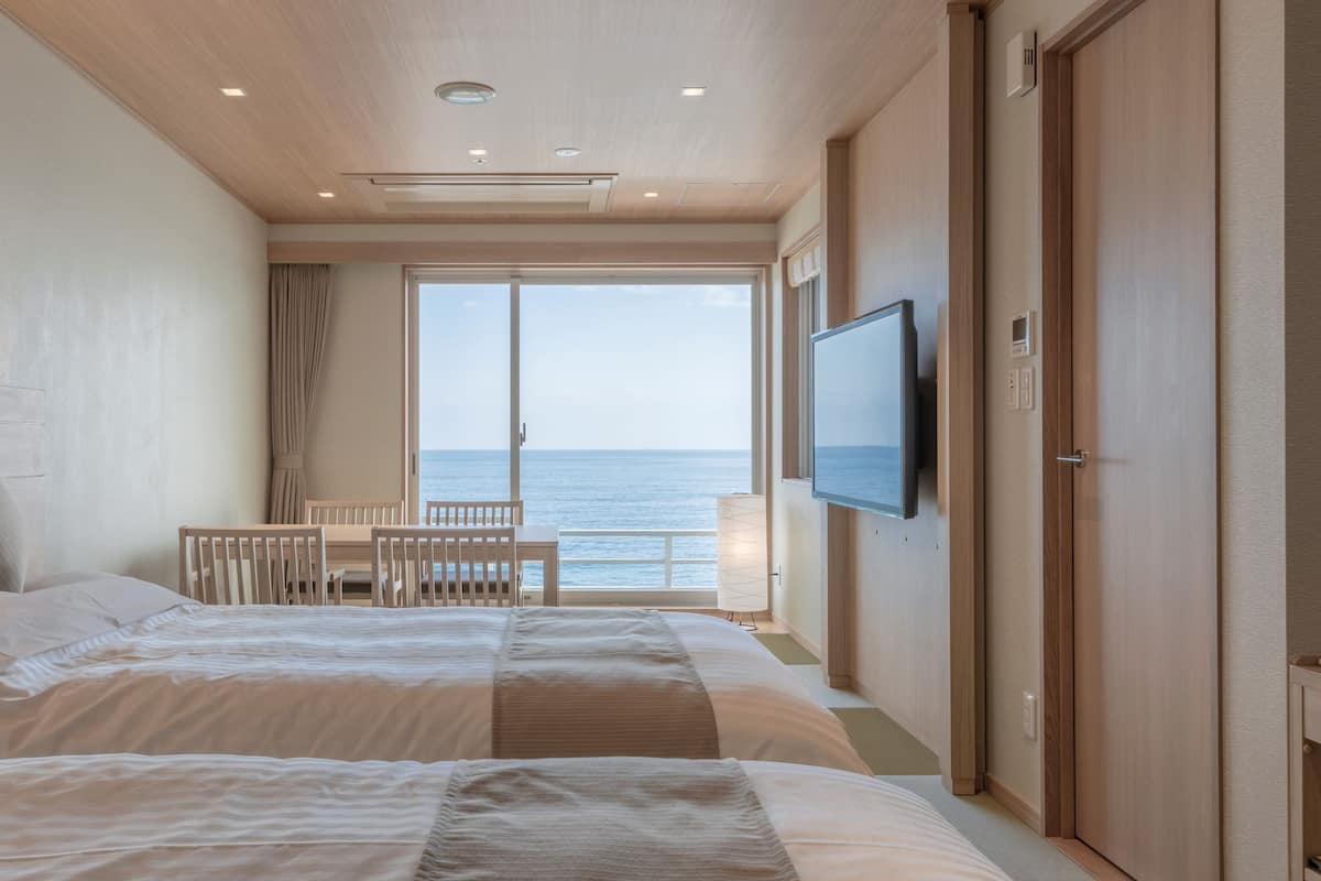 Een hotelkamer met een bed, een televisie, een bureau en uitzicht op zee.