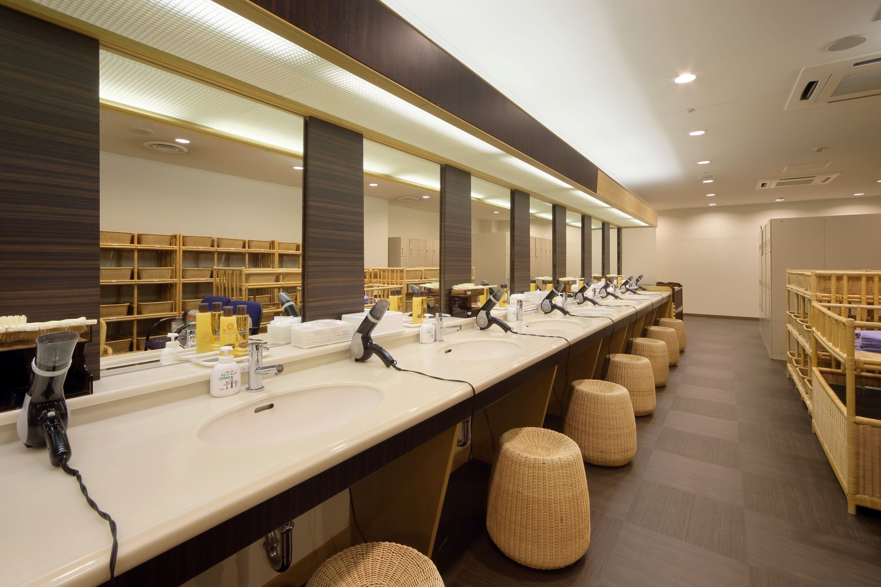 A long, modern bathroom with multiple sinks, mirrors, and wicker stools.