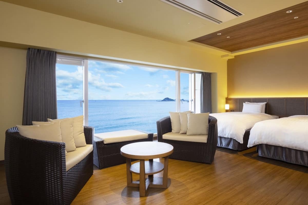 Een hotelkamer met twee bedden, een bank, een ronde tafel en een groot raam met uitzicht op zee.