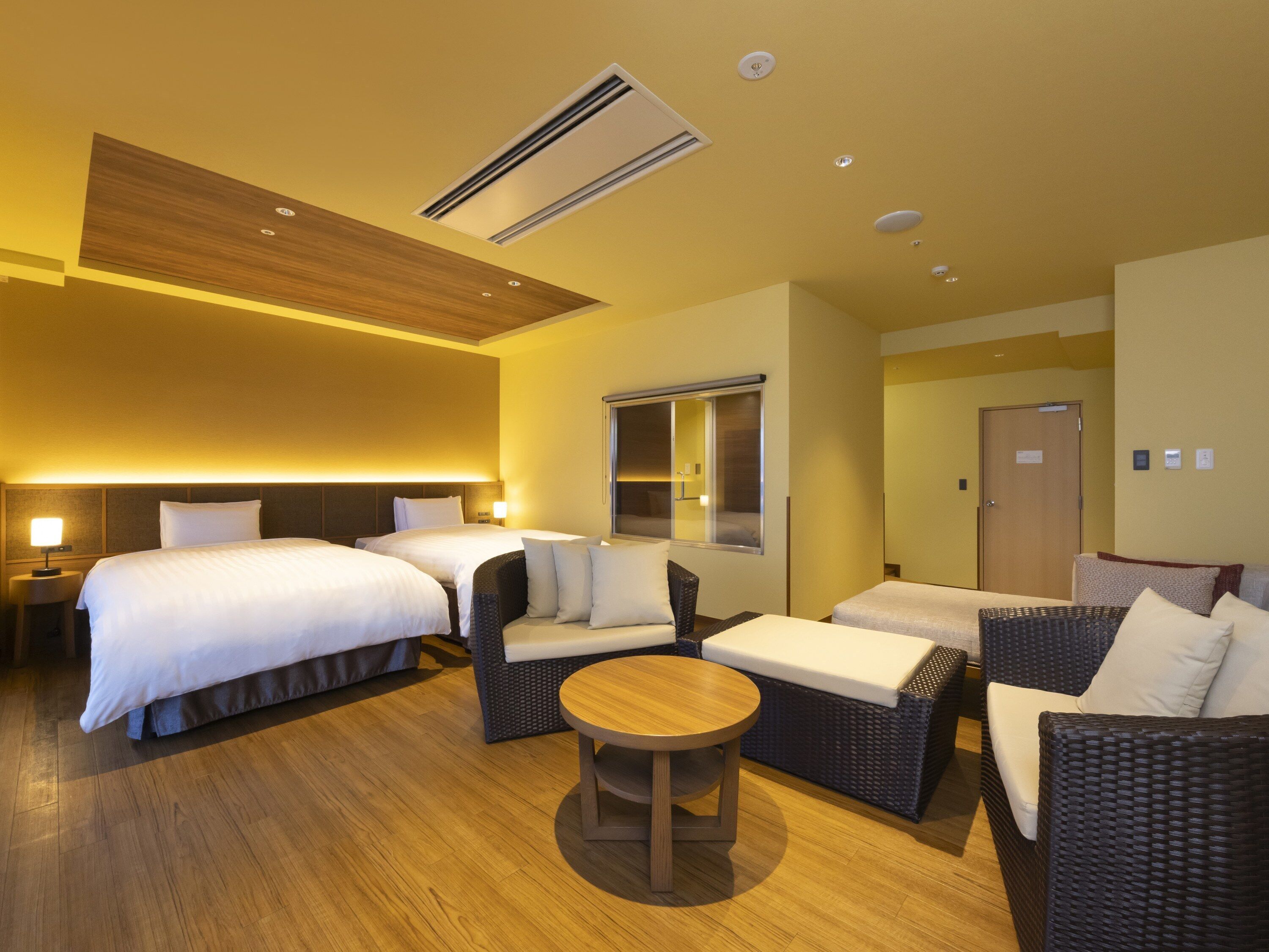 A hotel room with two beds, a sofa, a round table, and a window.