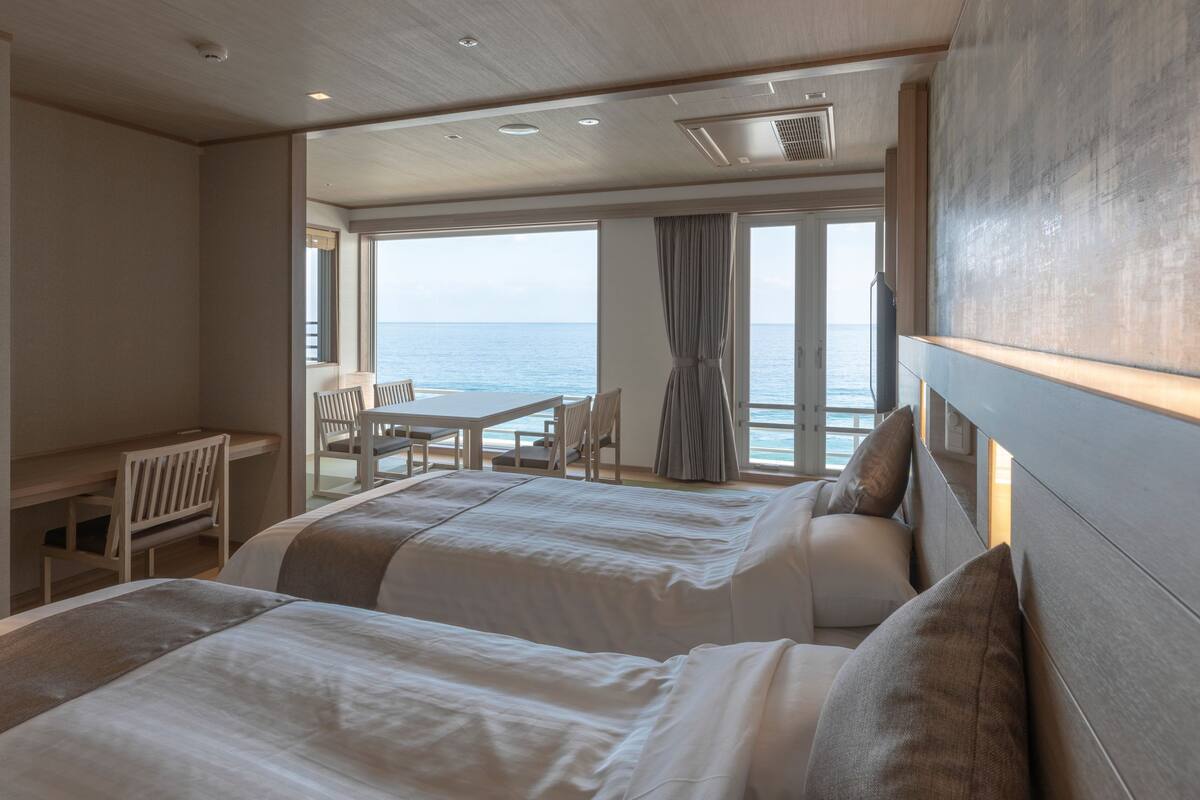 Een hotelkamer met twee bedden, een bureau en uitzicht op zee.
