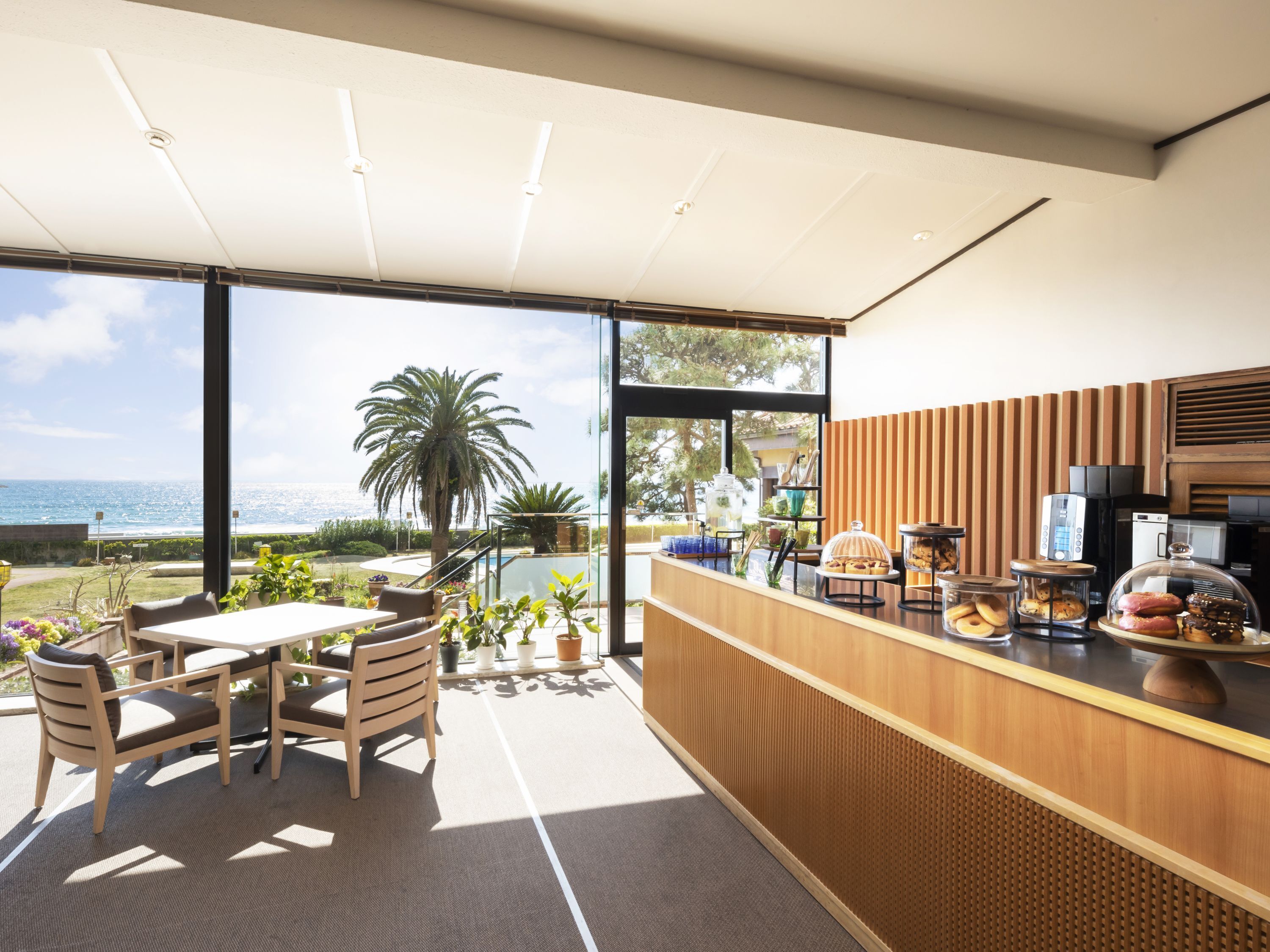 A modern kitchen with a view of the ocean, a dining area with a table and chairs, and a counter with various food items.