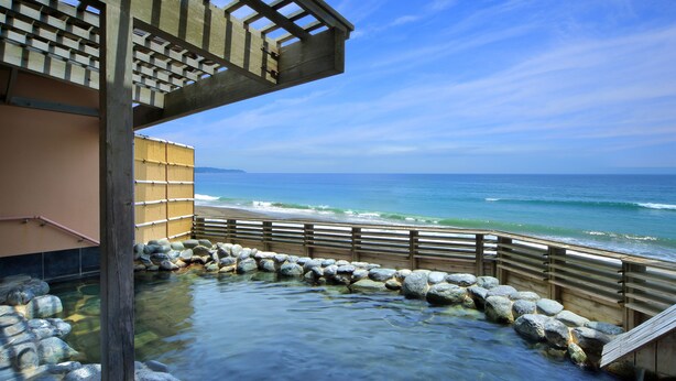 Ein traditionelles japanisches Onsen mit einer Holzterrasse und einem steinbelagten Weg zum Wasser.