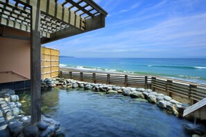 A traditional Japanese onsen with a wooden deck and stone pathway leading to the water. - Kamogawa Grand Hotel (Kamogawa)