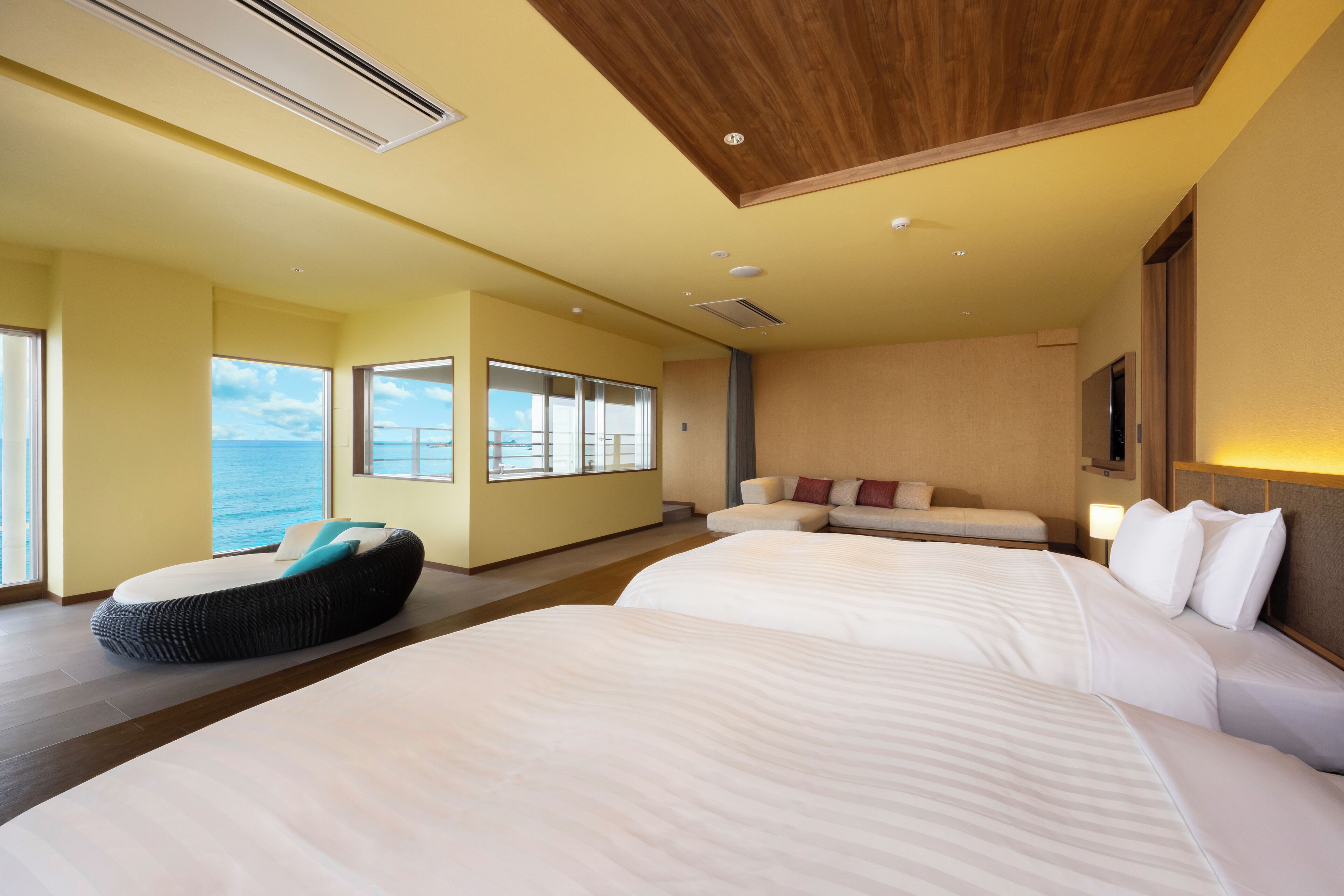 A modern hotel room with two large beds, a sofa, and a view of the sea.