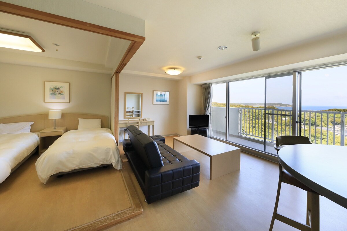 Une chambre d’hôtel avec deux lits, un canapé, un bureau, une télévision et un balcon avec vue.