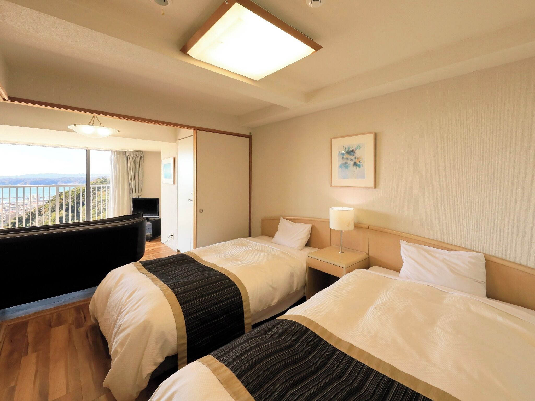 Ein Hotelzimmer mit zwei Betten, einem Fernseher, einem Balkon mit Blick und einem Bild an der Wand.