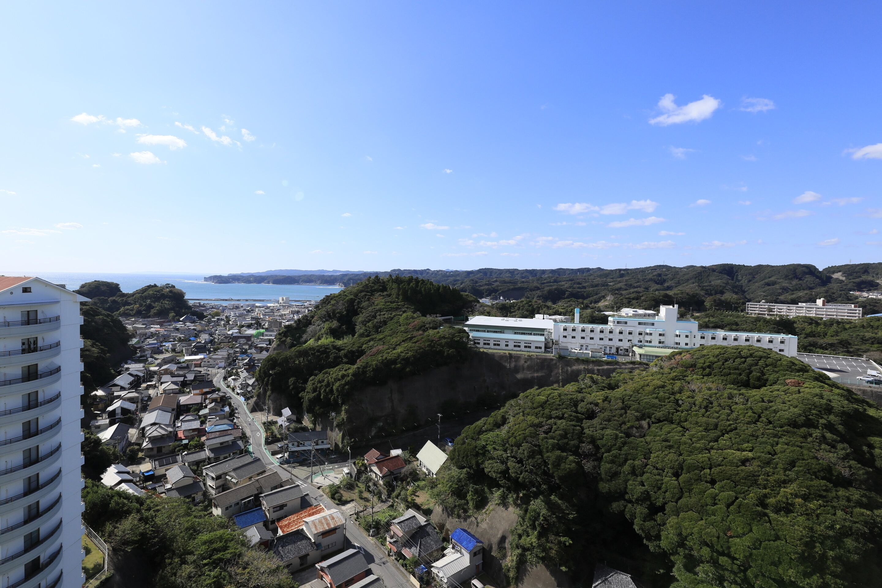 A coastal town with a mix of residential and commercial buildings, a prominent white building, and lush green hills.