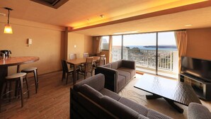 A modern hotel room with a dining area, sofa set, flat-screen TV, and a balcony with a city view. - Katsuura Hilltop Hotel & Residence (Katsuura)
