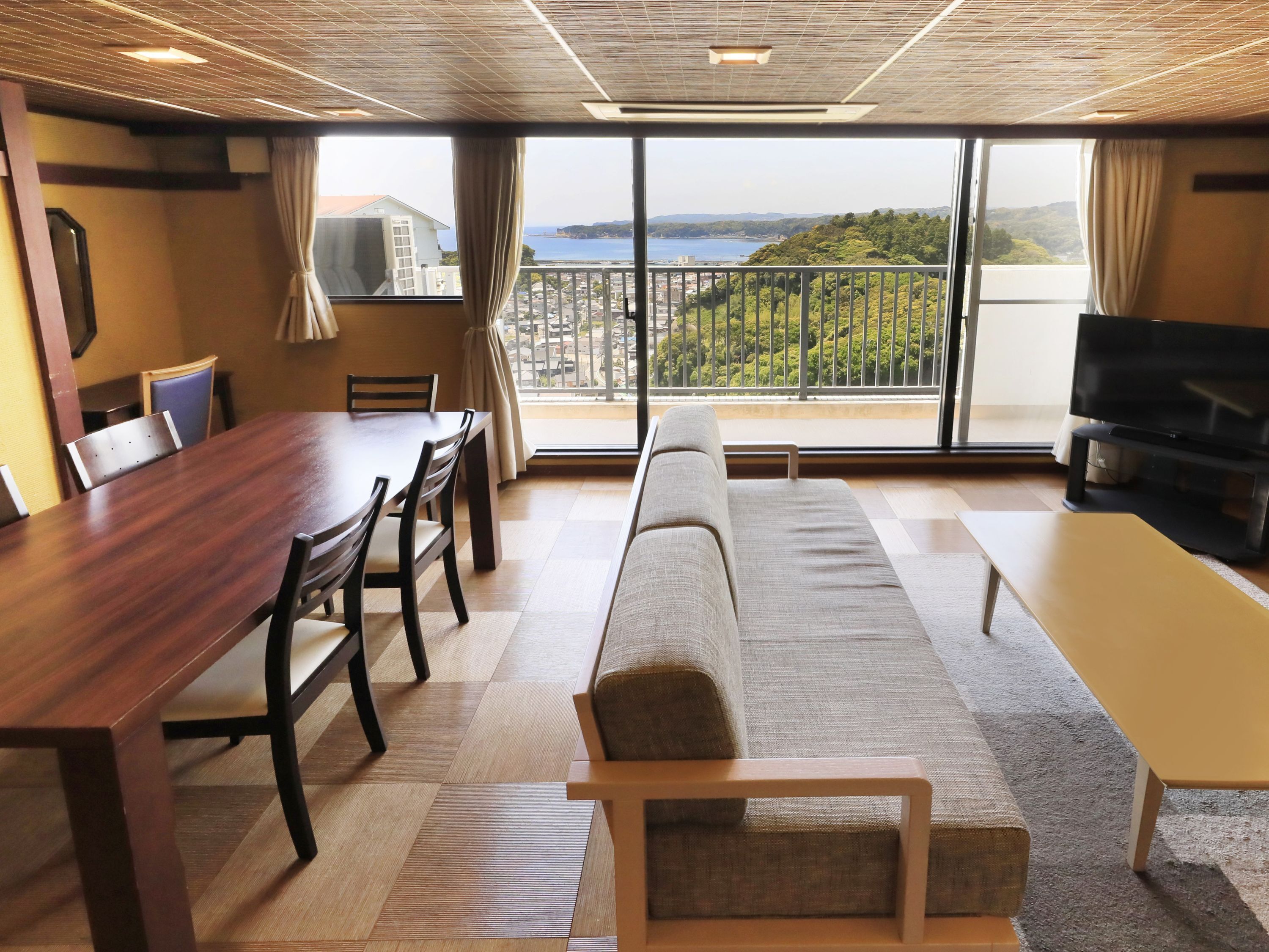 Una sala de estar moderna con comedor, sofá, televisor y balcón con vistas a la ciudad y las colinas.