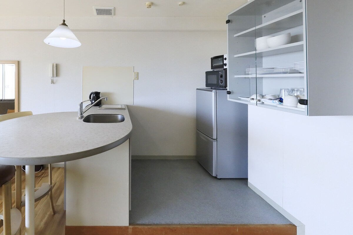 Une cuisine compacte avec un îlot central rond, un réfrigérateur et un four à micro-ondes placés sur le dessus.