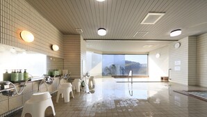 A modern indoor pool area with tiled floors, white stools, and a large window offering a view of the outdoors. - Katsuura Hilltop Hotel & Residence (Katsuura)