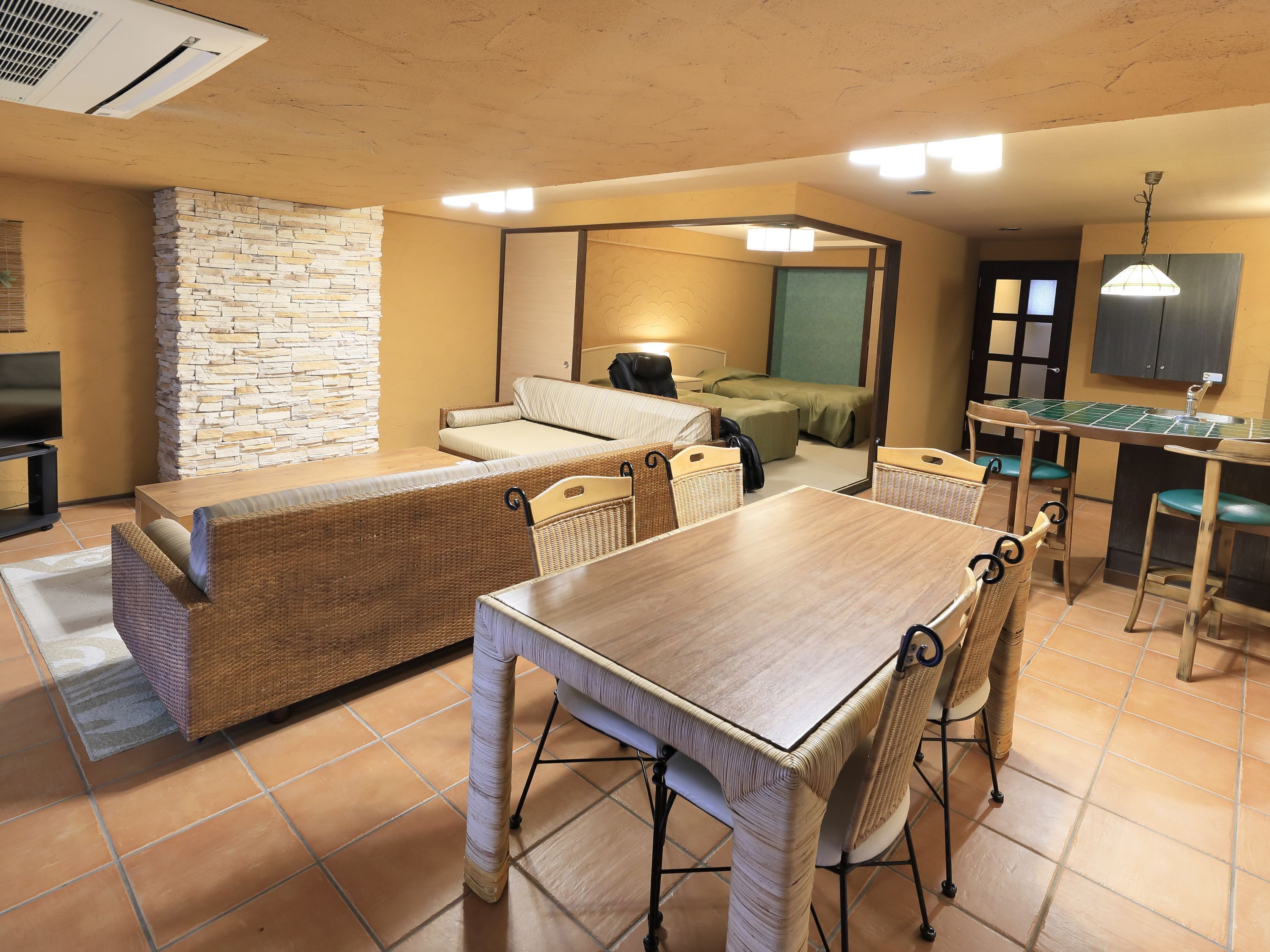 A hotel room with a dining area, a sofa, a TV, and a stone wall.