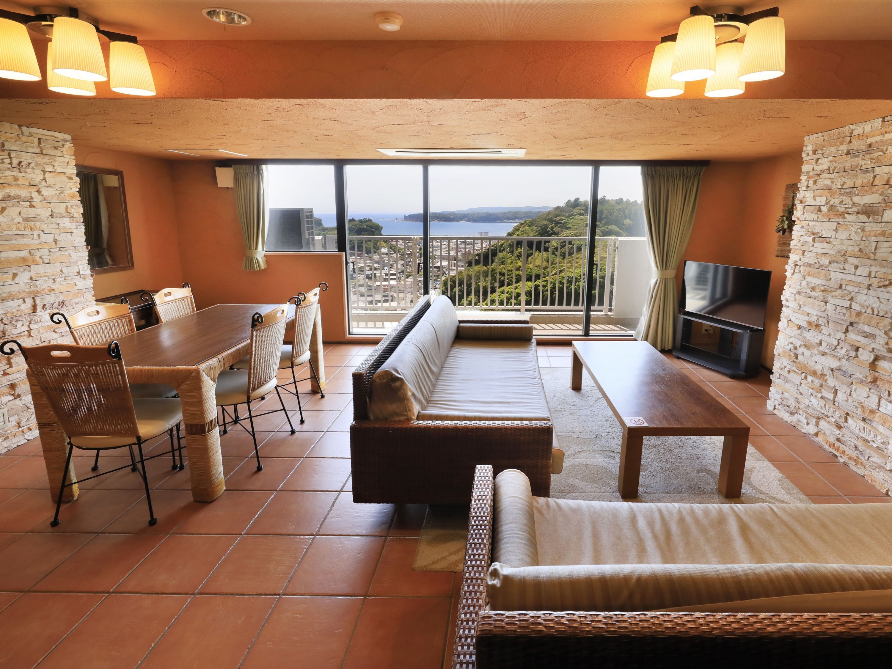 A spacious room with a dining area, sofa, and a balcony with a view.