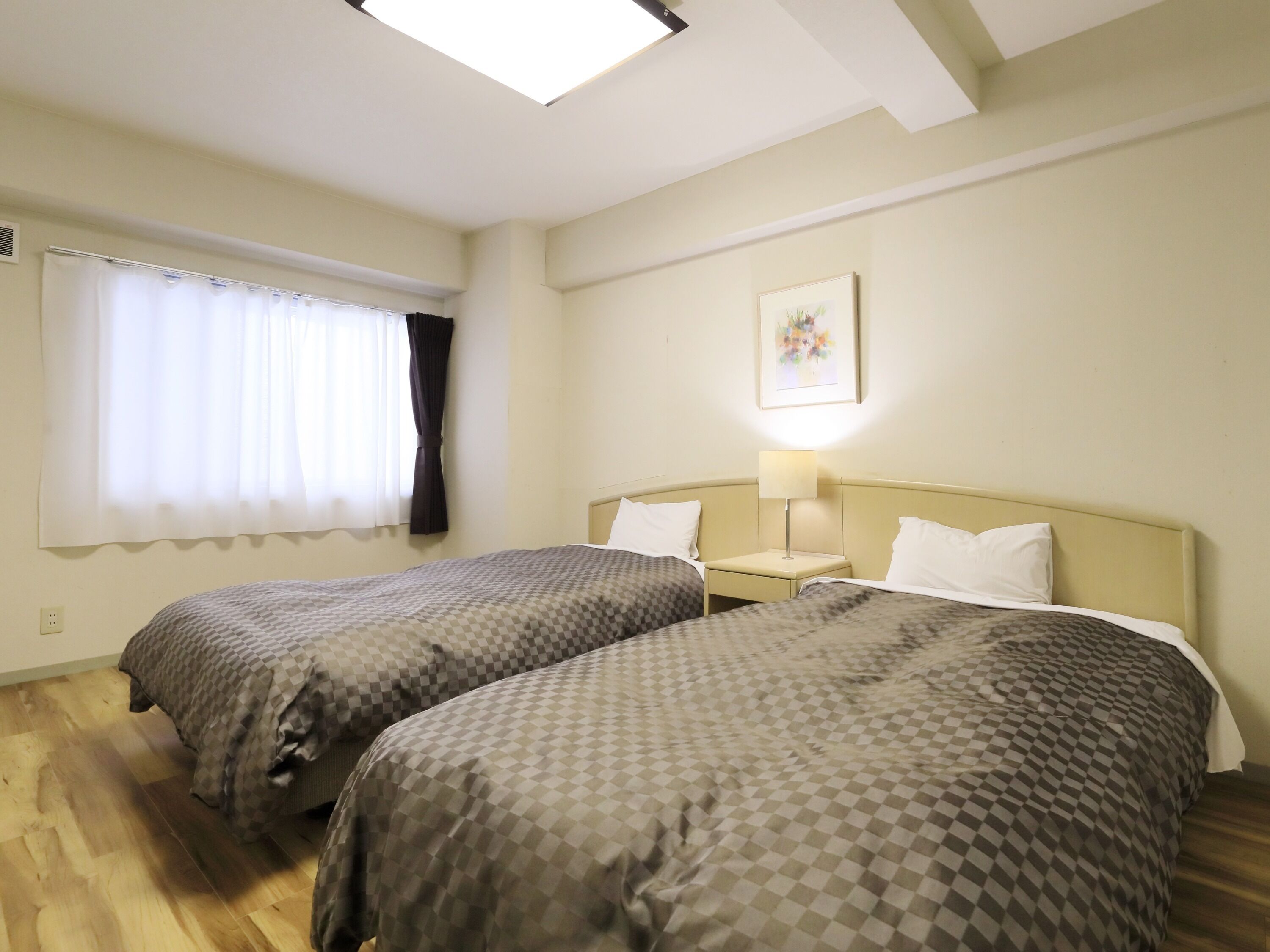 Habitació d'hotel amb dos llits, una finestra amb cortines, una làmpada de nit i un quadre al mur.