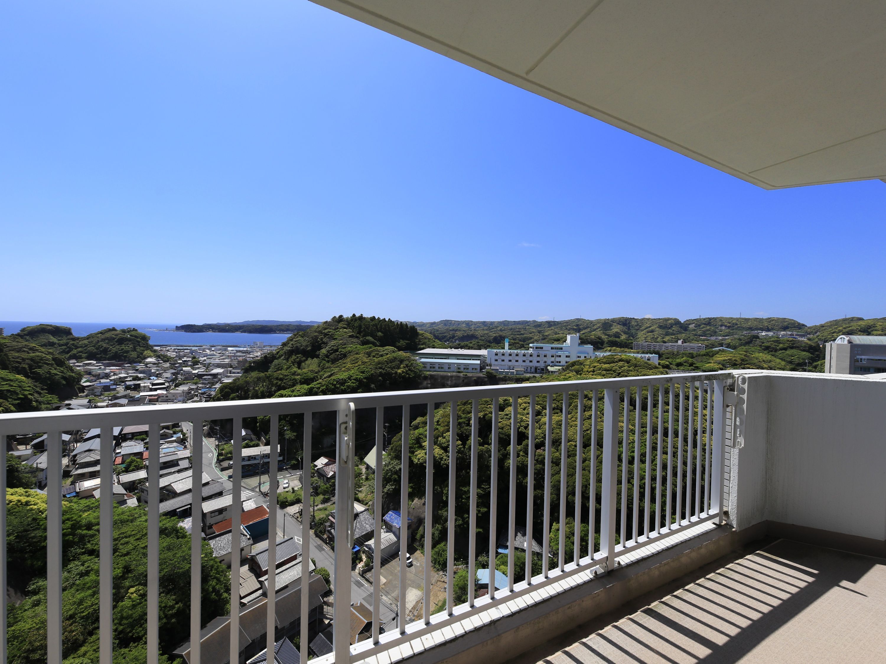 A balcony with a view of a residential area, a body of water, and distant hills.