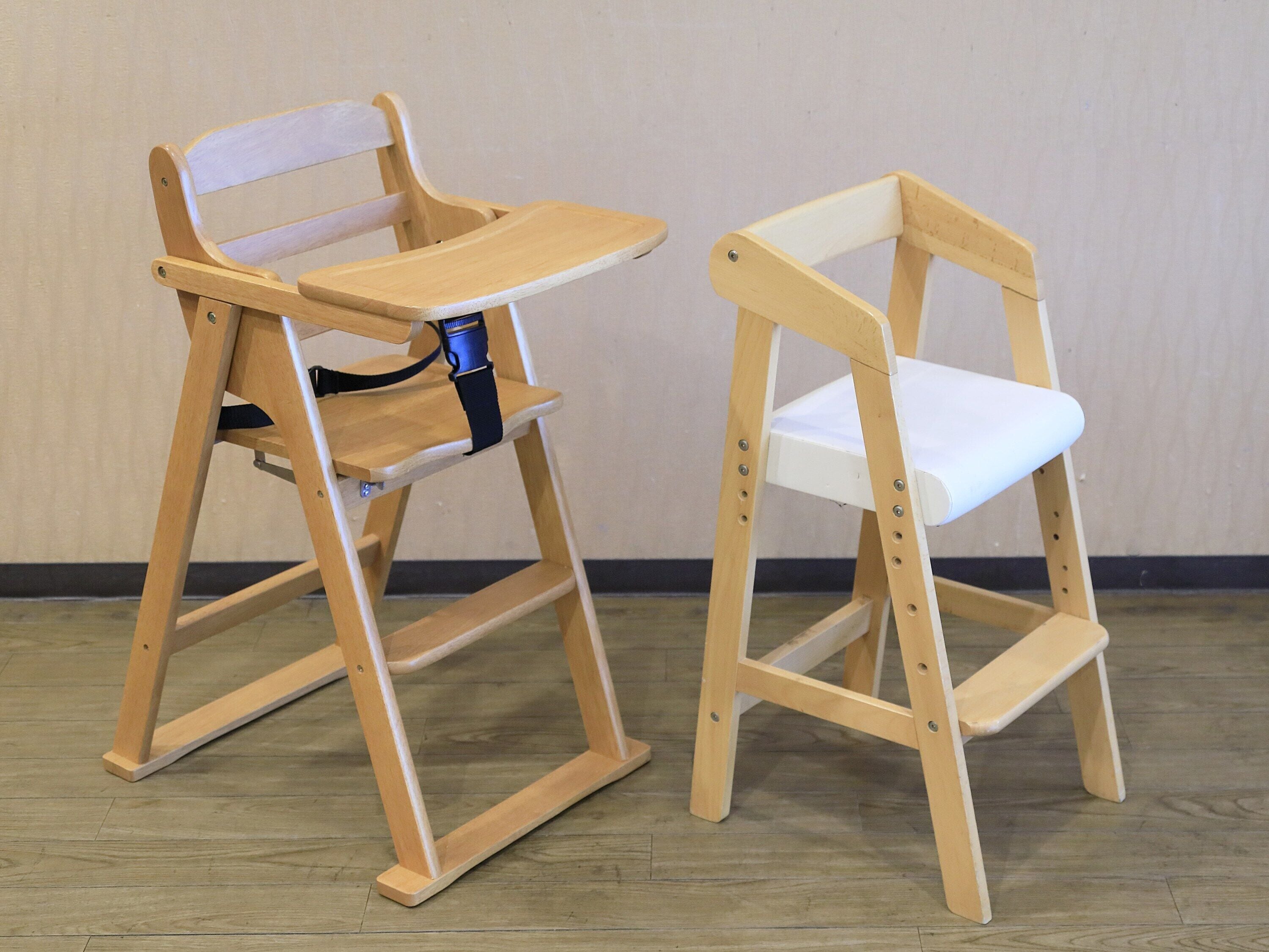 Deux rehausses pour enfants en bois, équipées d’un plateau, l’une avec une sangle bleue et l’autre avec un plateau blanc.