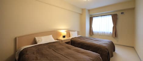 A hotel room with two beds, a nightstand with a lamp, a ceiling fan, and a window with curtains.